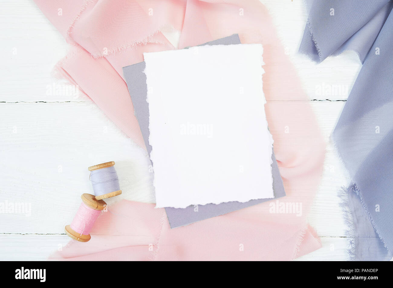 Carte vierge blanc sur un fond de tissu rose et bleu sur fond blanc. Immersive avec enveloppe et carte vierge. Mise à plat. Vue d'en haut Banque D'Images