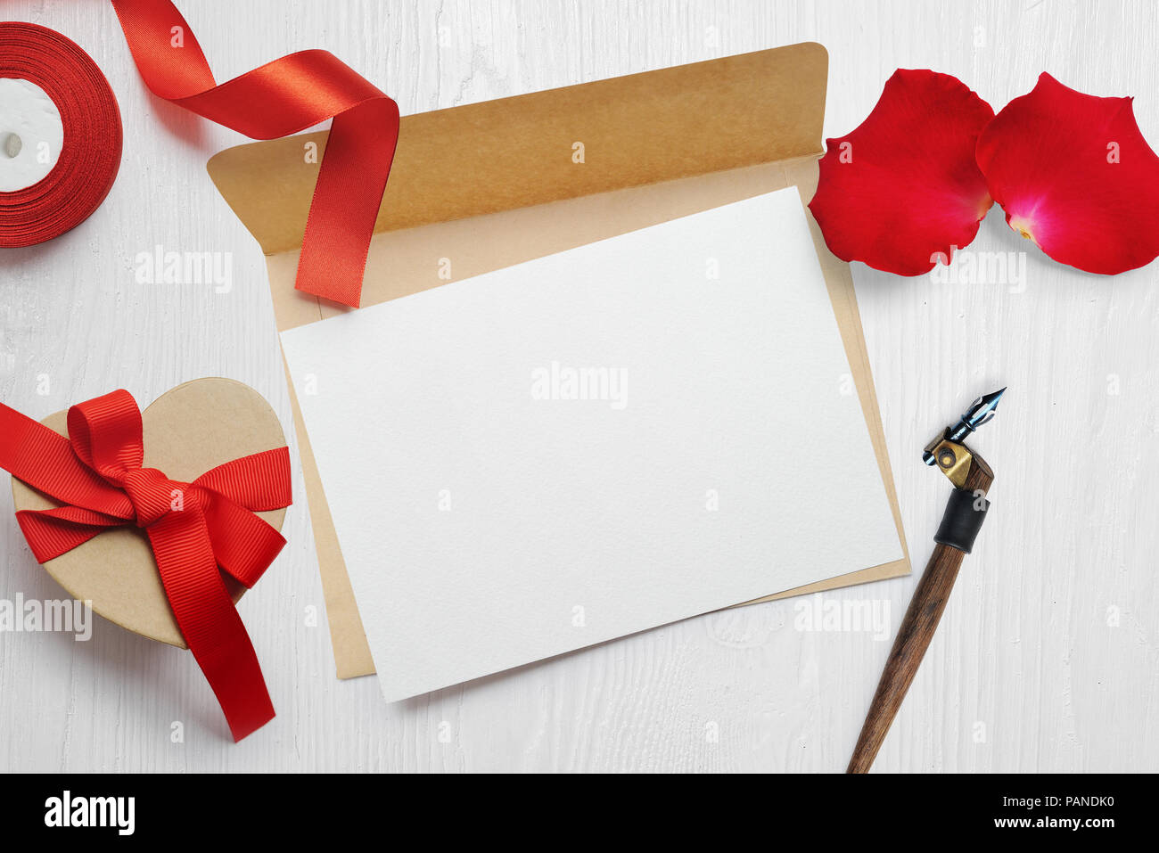 Immersive Valentines Day Greeting card lettre dans l'enveloppe avec boîte cadeau kraft ruban rouge, plat déposer sur un fond en bois blanc, avec place pour votre texte, haut voir photo maquette Banque D'Images