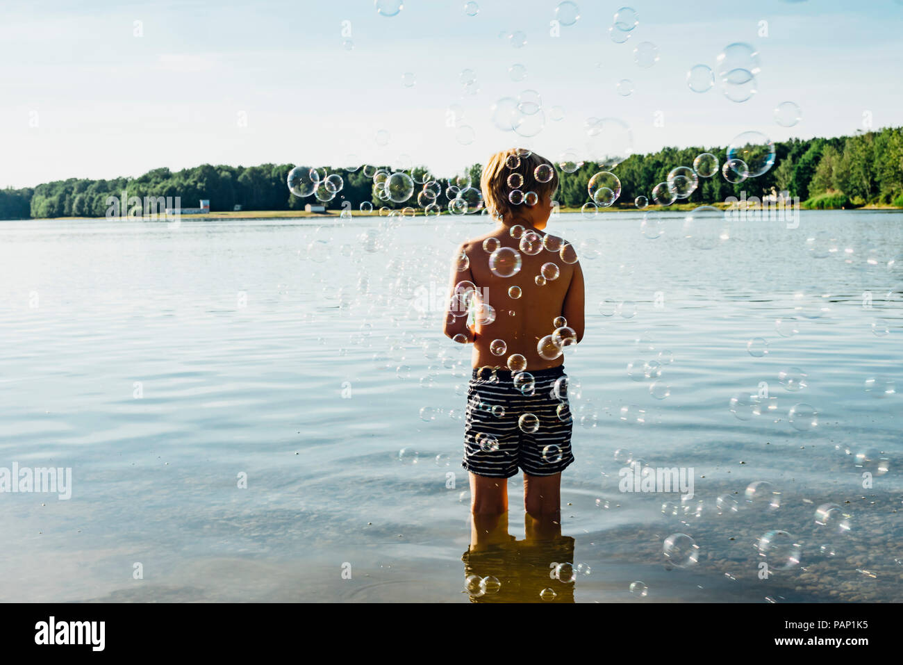 Garçon dans un lac entouré par des bulles de savon Banque D'Images