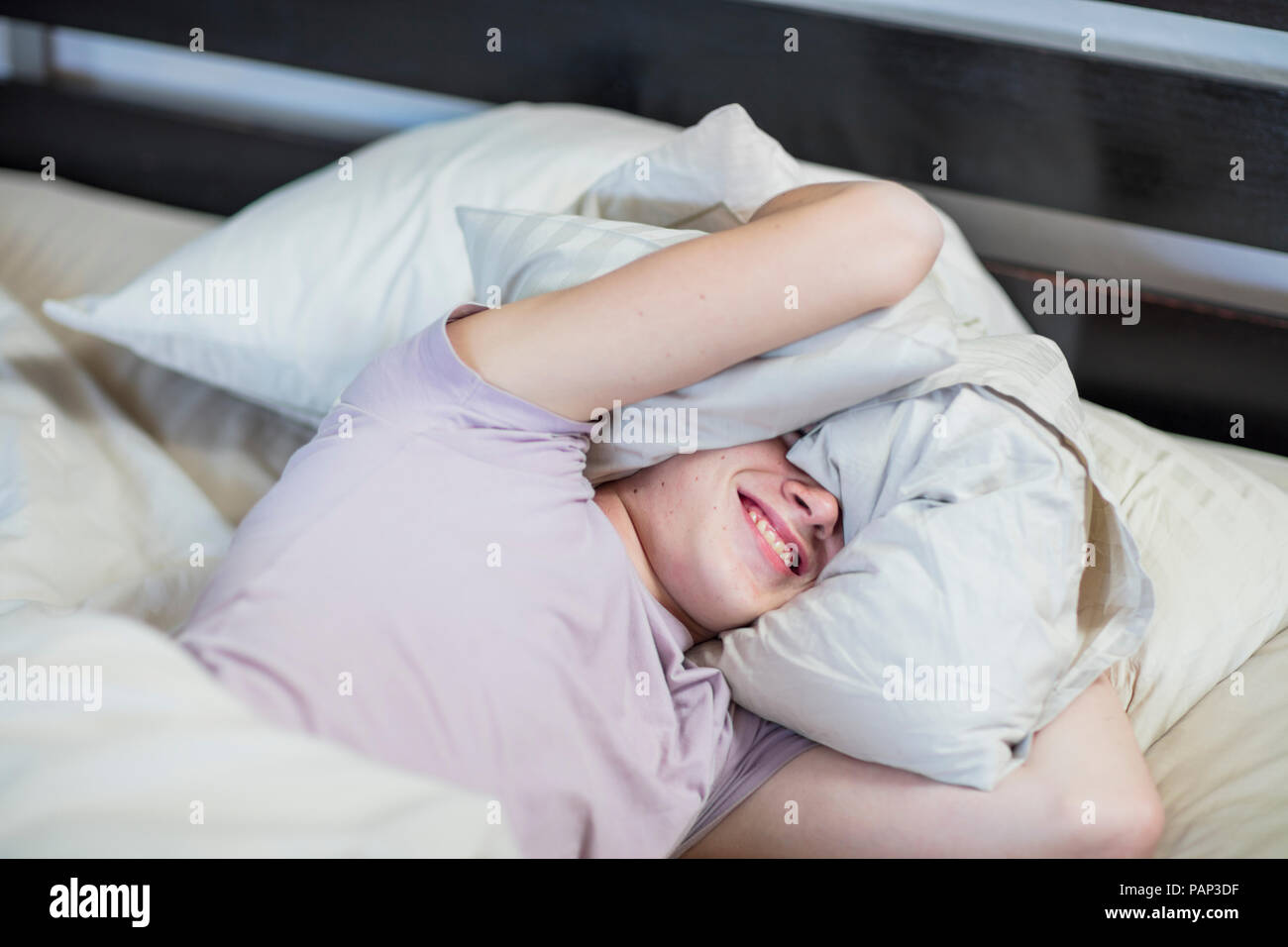 Boy Lying in Bed holding oreiller sur sa tête Banque D'Images