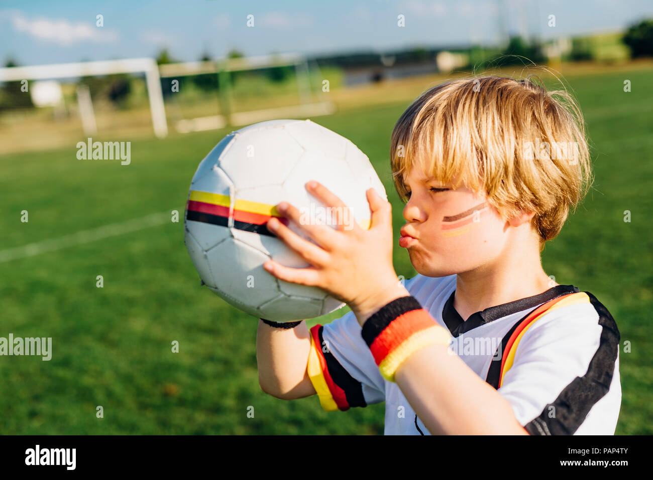 Garçon avec la peinture pour le visage et maillot de football allemand, kissing soccer ball Banque D'Images