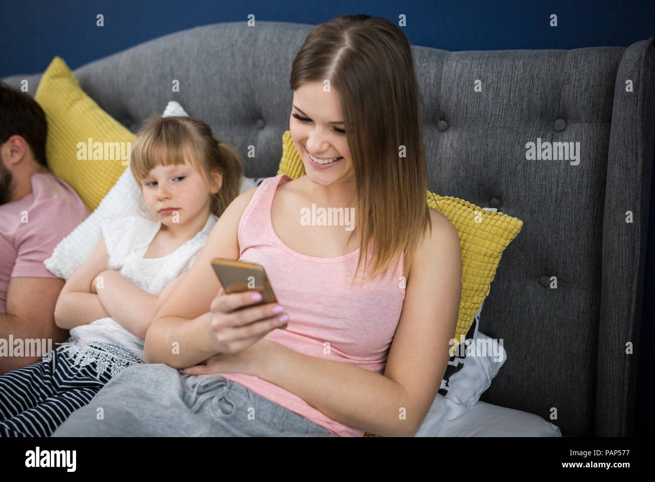 Négligé petite fille assise sur le lit avec ses parents, using smartphones Banque D'Images