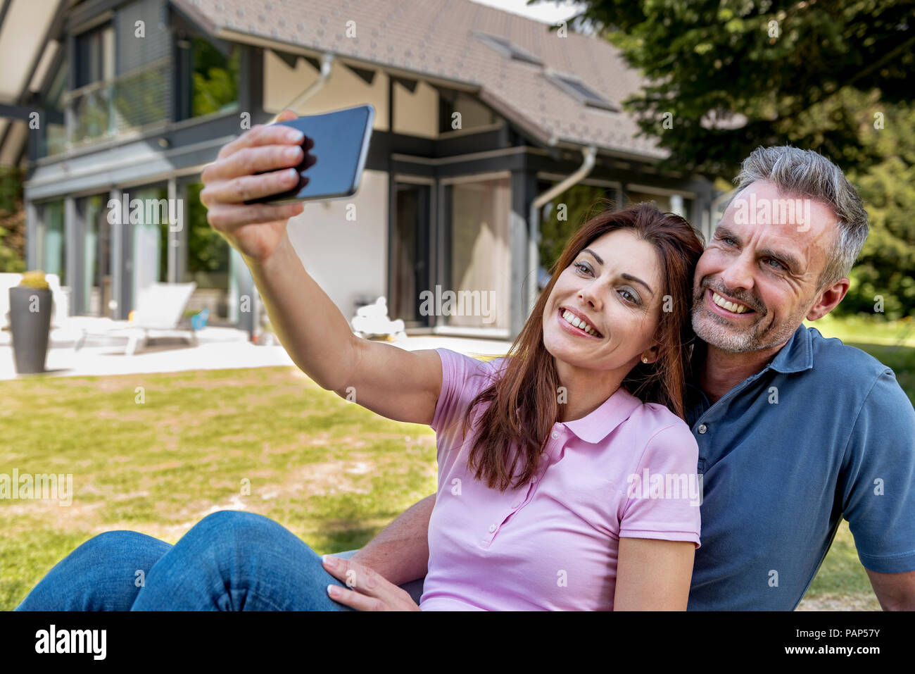 Heureux couple assis dans le jardin de leur maison en prenant un selfies Banque D'Images