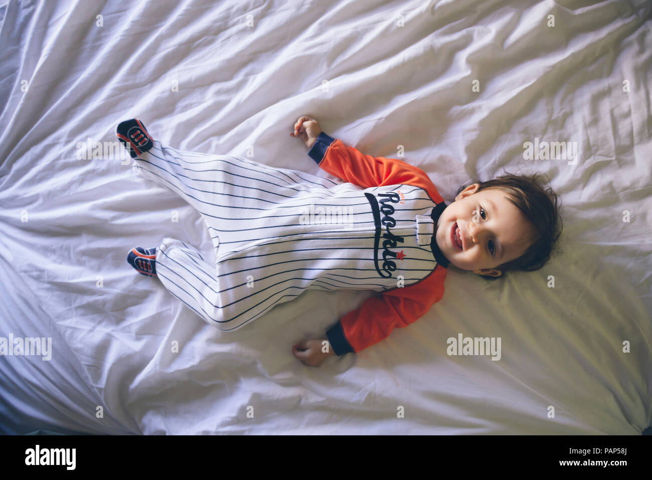 Portrait of smiling baby girl wearing jumpsuit lying on bed Banque D'Images