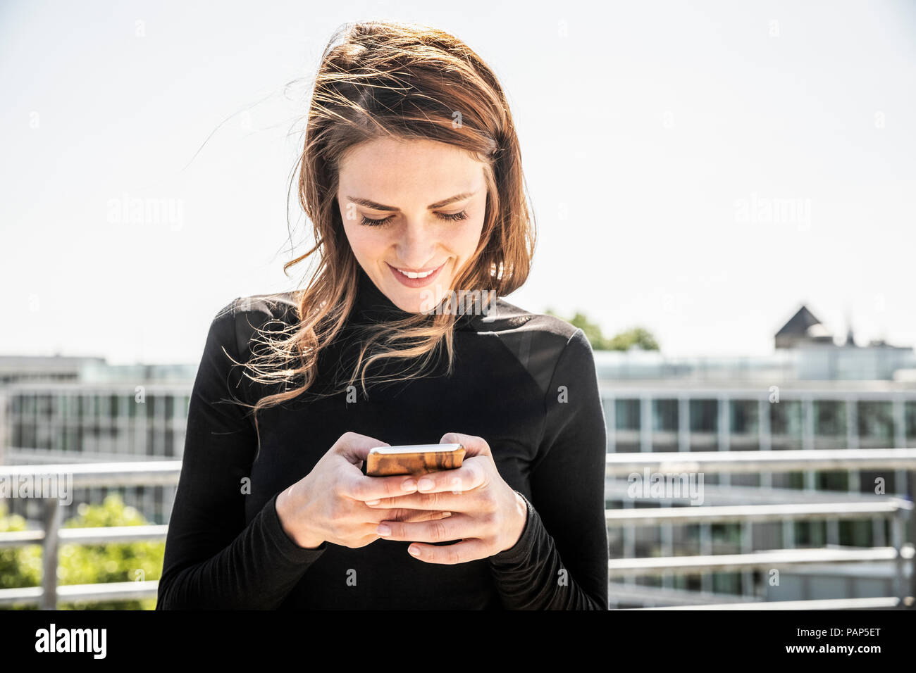 Smiling woman text messaging sur la terrasse du toit Banque D'Images