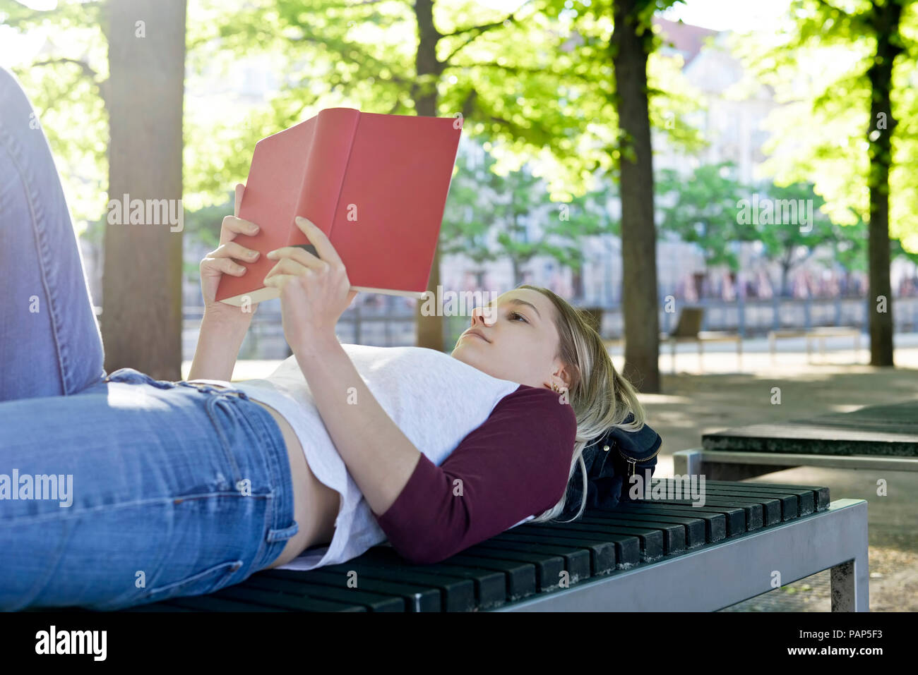 Jeune femme lisant un livre sur un banc Banque D'Images