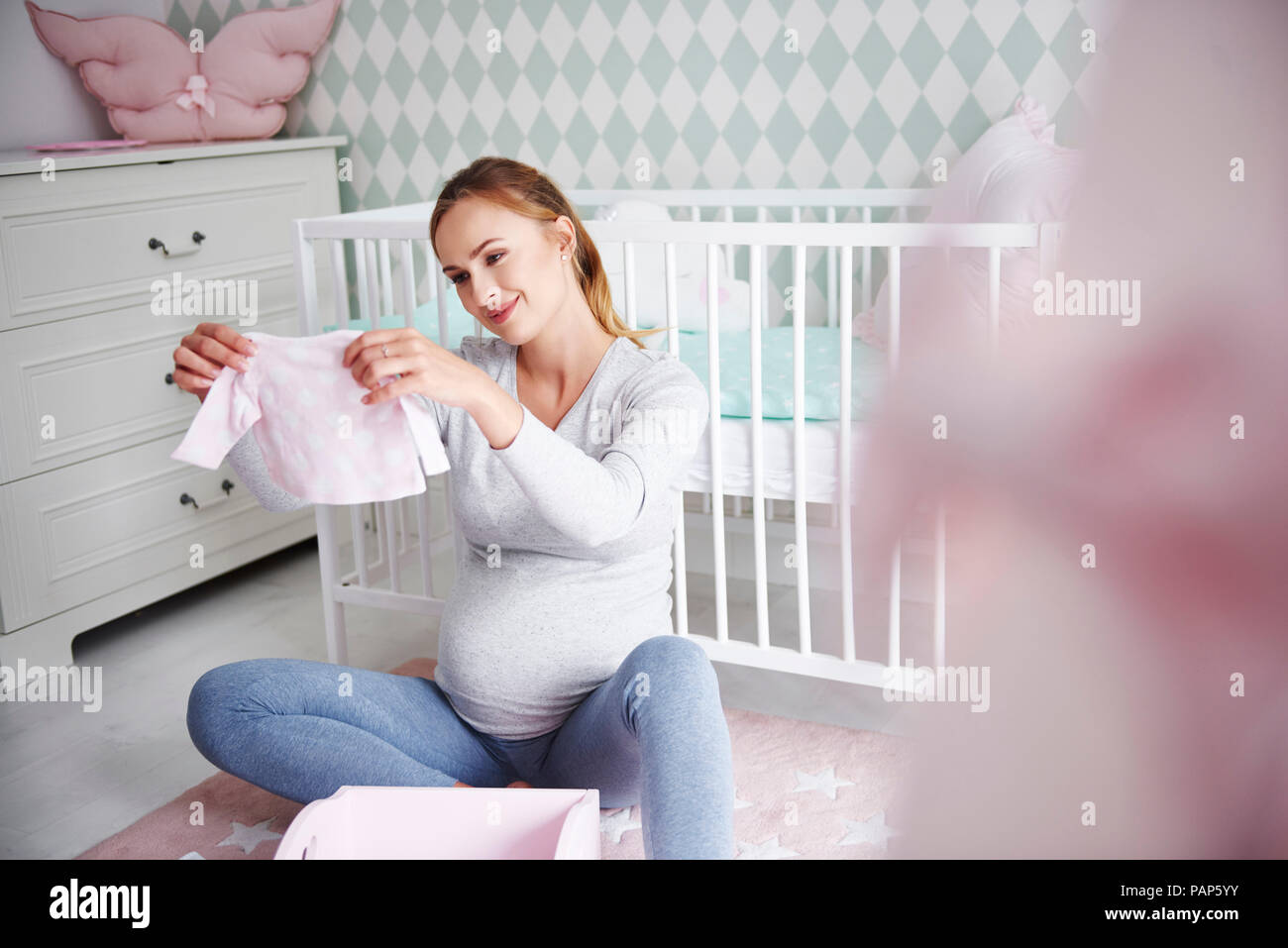 Femme enceinte avec les vêtements de bébé dans la chambre de bébé Banque D'Images