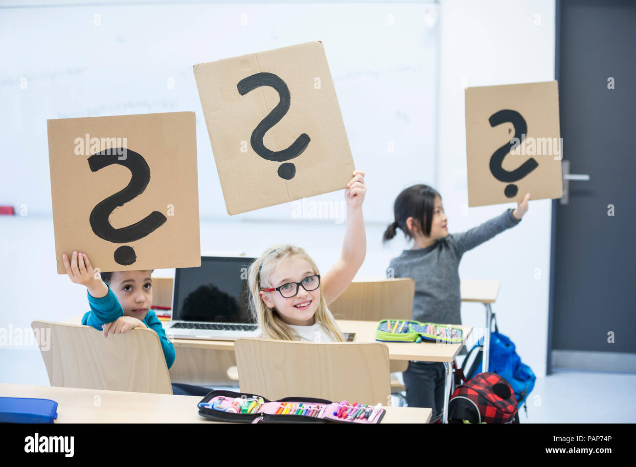 Ordinateur portable avec les élèves en classe holding up cartons avec des points d'interrogation Banque D'Images