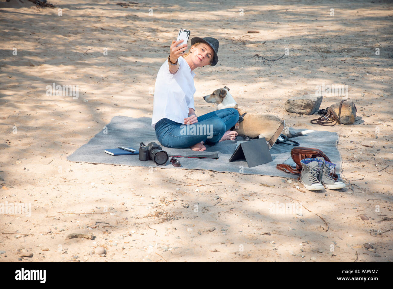 Femme assise sur couverture sur plage avec un chien selfies Banque D'Images