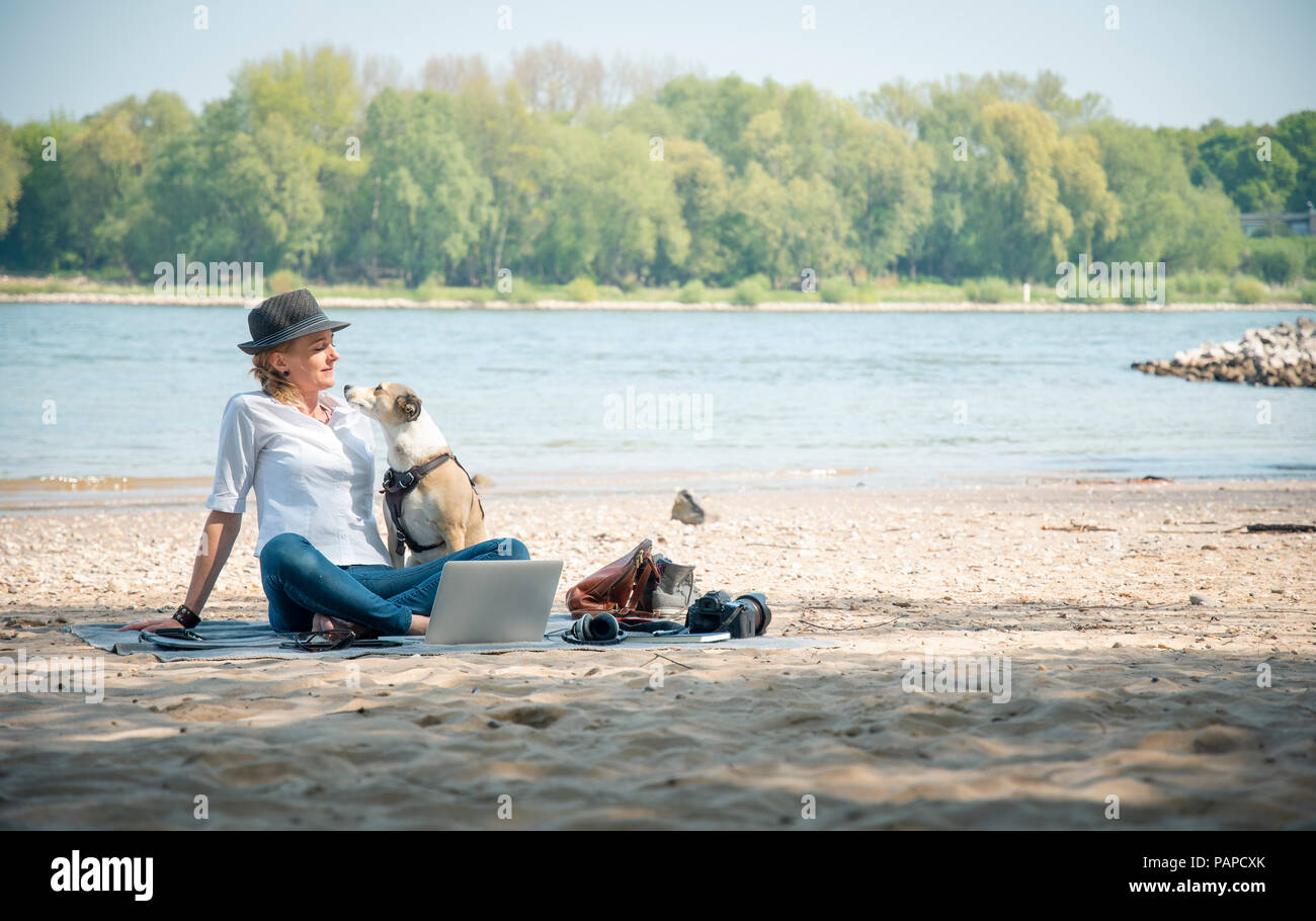 Femme assise sur couverture à une rivière avec chien et coffre Banque D'Images