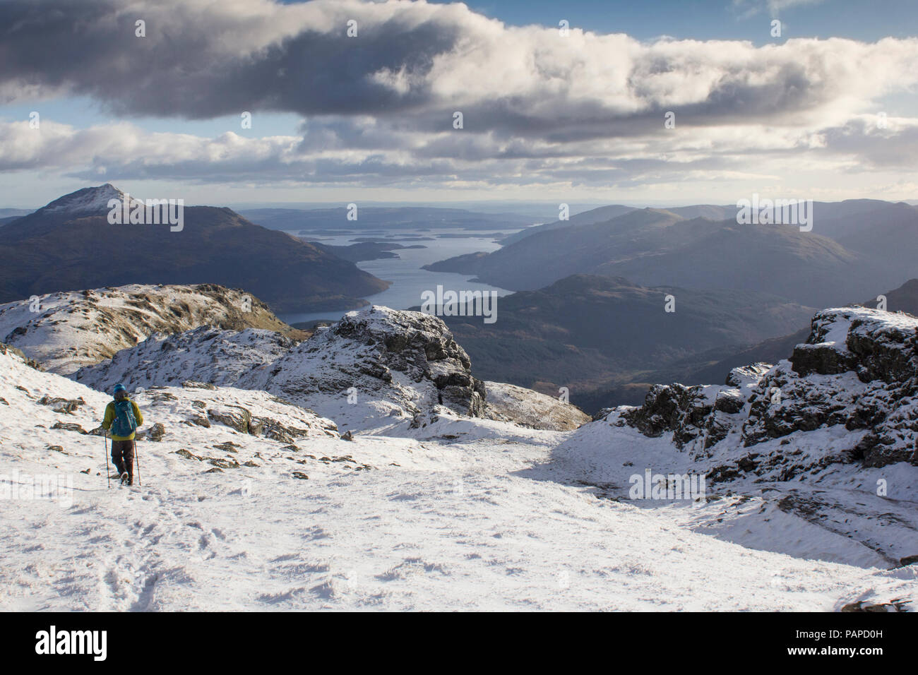 Un grimpeur escalade la montagne couverte de neige en hiver, Ben Vorlick avec Ben Lomond et les Trossachs de montagnes en vue. L'Écosse. Banque D'Images