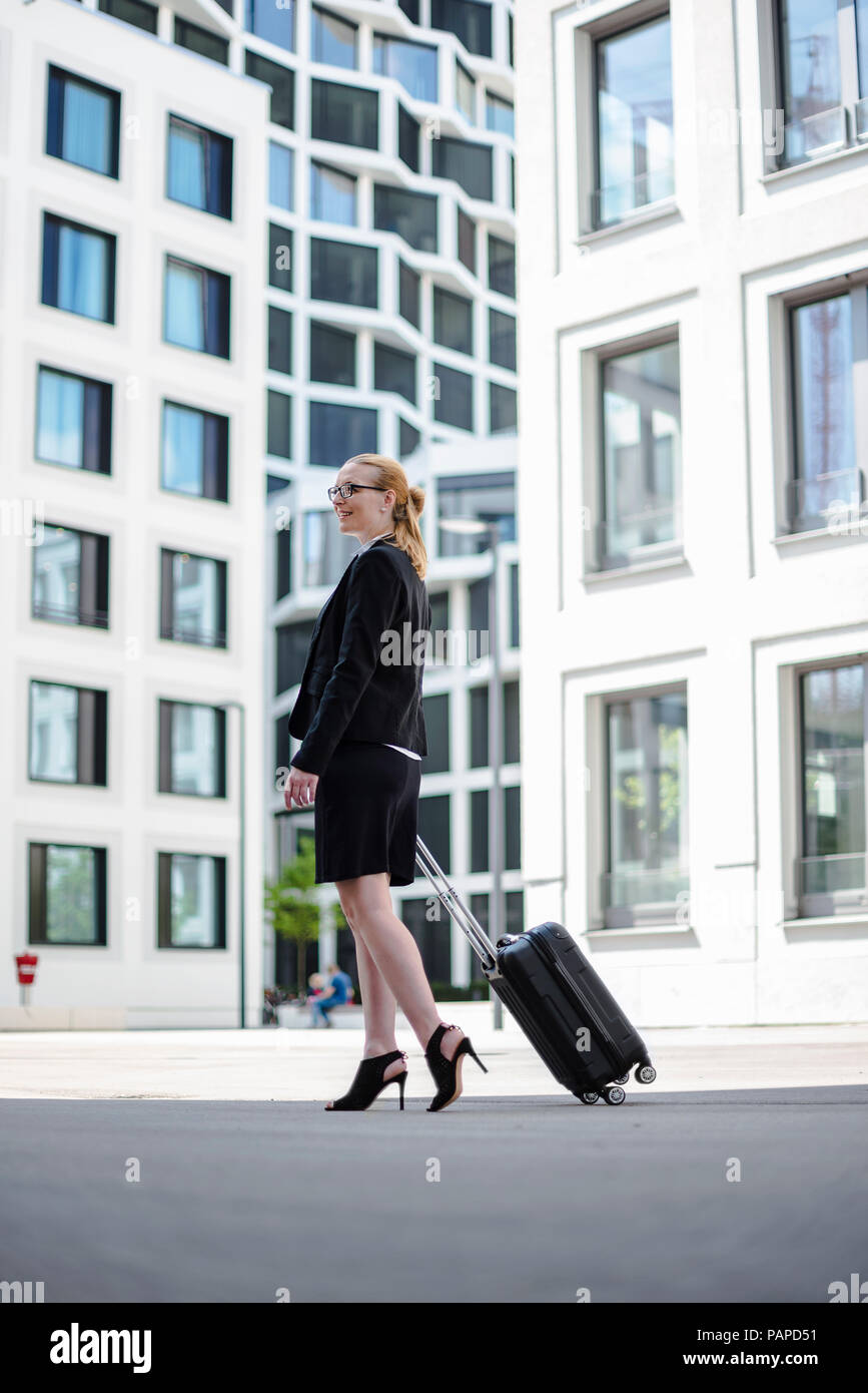 Mature businesswoman with suitcase walking en face d'immeubles de bureaux Banque D'Images