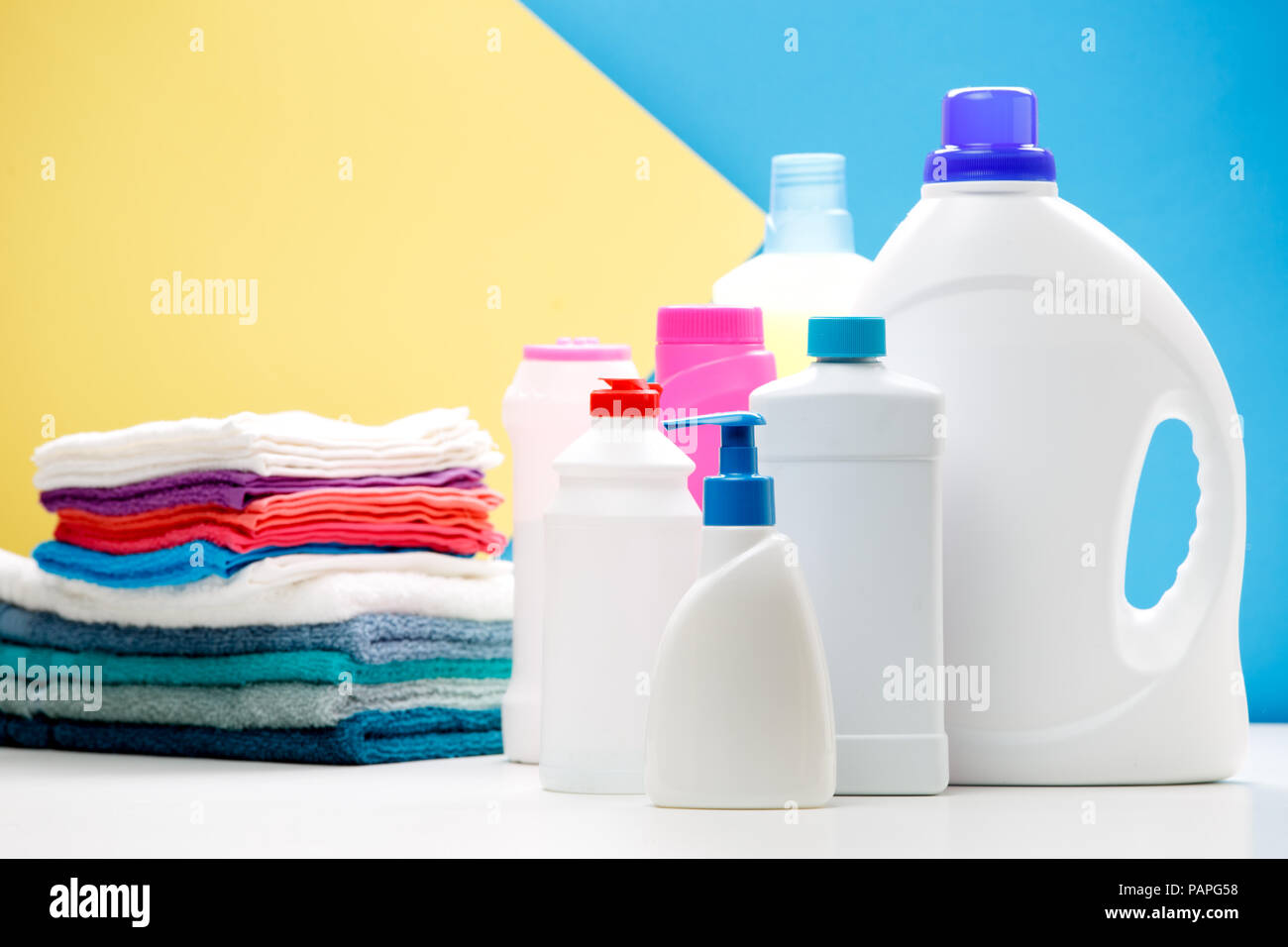 Photo de plusieurs bouteilles de produits de nettoyage et les serviettes de couleur sur la table isolé sur fond jaune, bleu, lieu d'inscription Banque D'Images