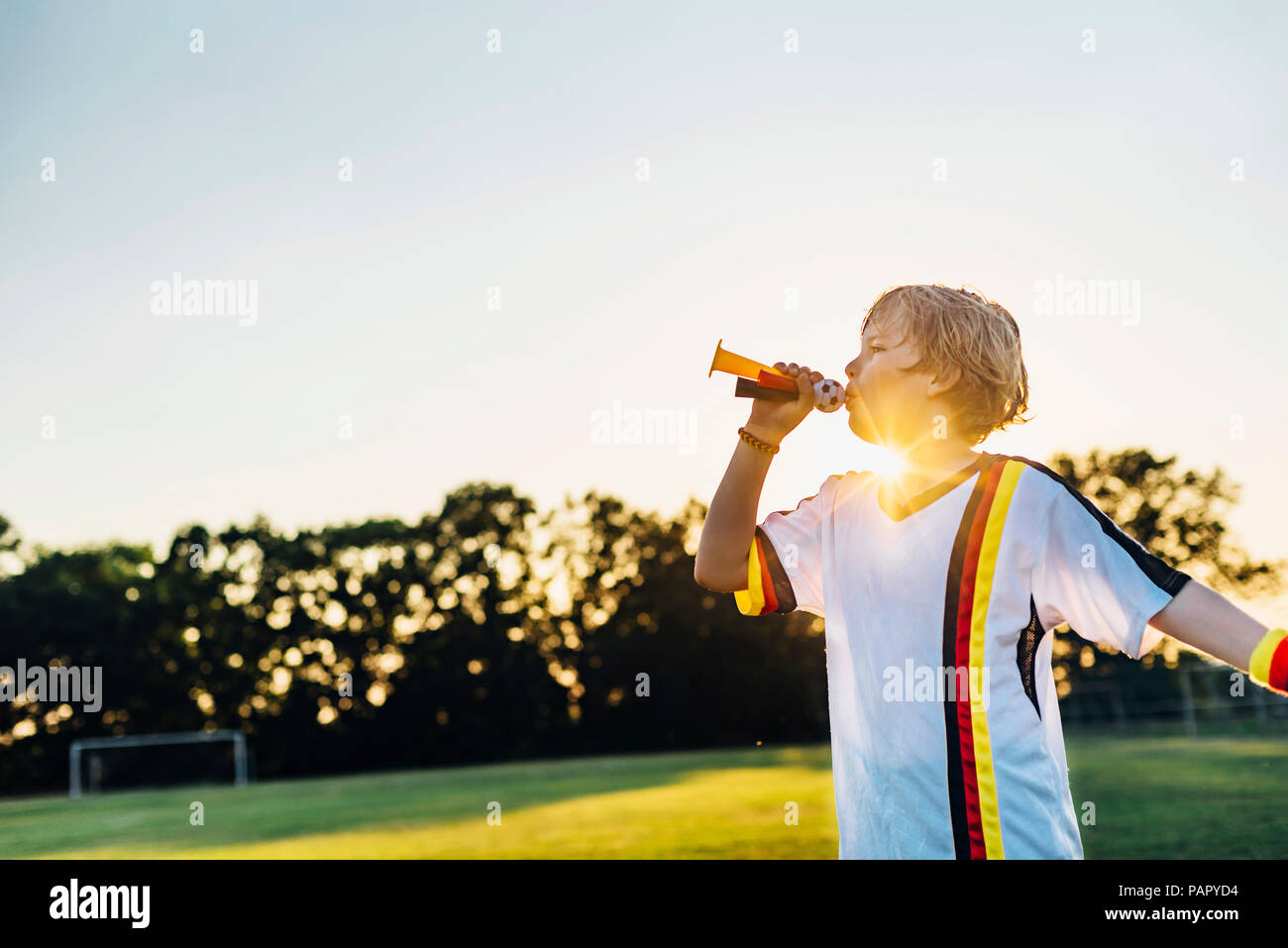 Boy wearing German soccer shirt, soufflant cornes sur terrain de football Banque D'Images