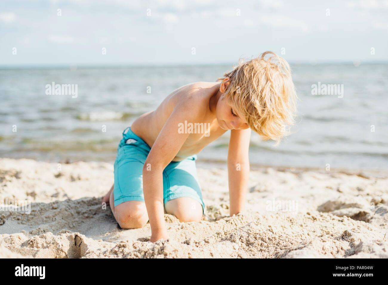 Garçon Blond jouer avec du sable sur la plage Banque D'Images