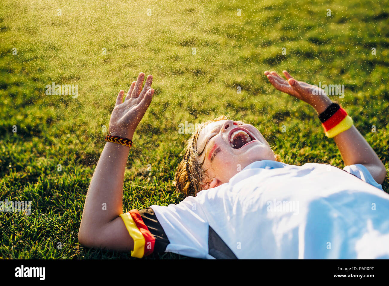 Garçon en allemand soccer shirt allongé sur l'herbe, rire et crier Banque D'Images