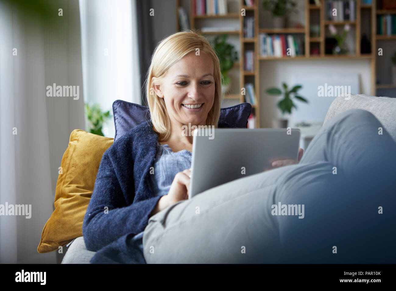 Woman using digital tablet, relaxing on couch Banque D'Images