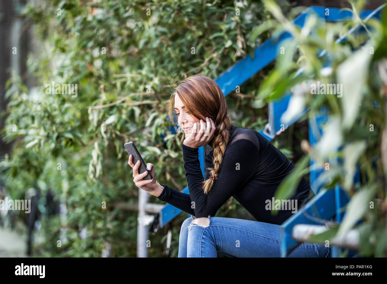Smiling woman sitting on stairs looking at smartphone Banque D'Images