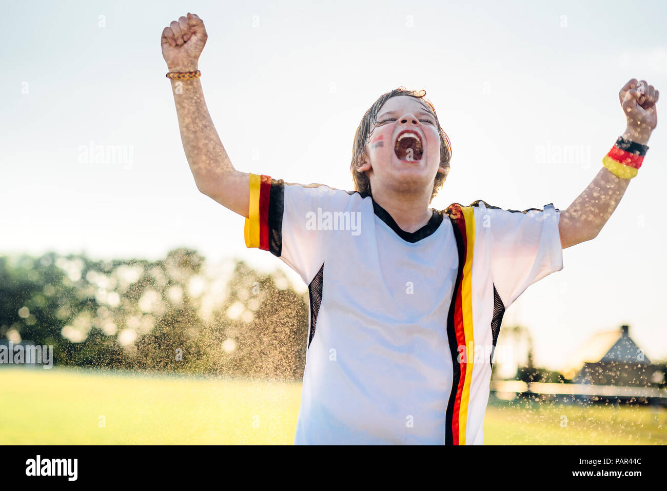 Boy wearing German soccer shirt crier de joie, debout dans les projections d'eau Banque D'Images