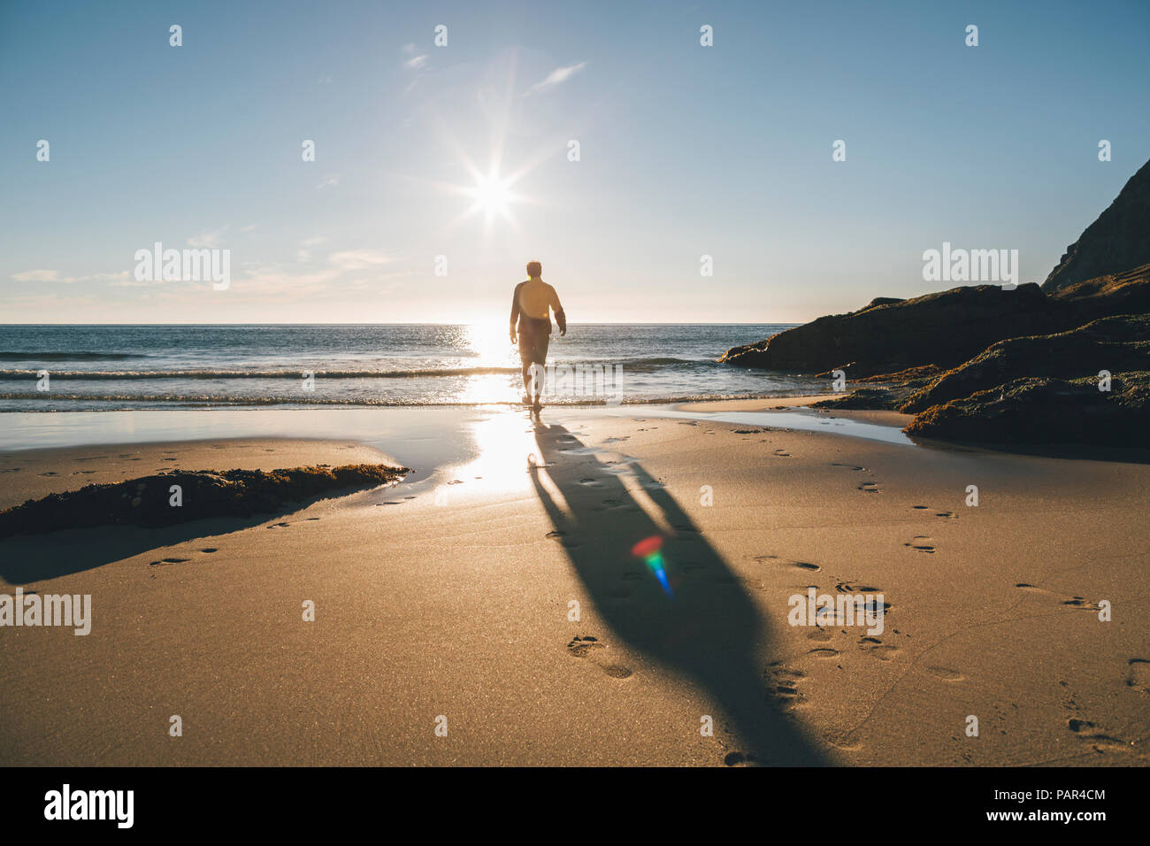 La Norvège, les îles Lofoten, Moskenesoy, homme qui marche dans le soleil à Kvalvika Beach Banque D'Images