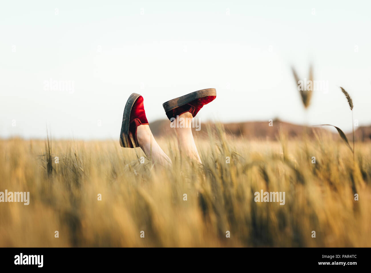 Femme couchée dans un champ, battre des jambes avec des chaussures rouges Banque D'Images