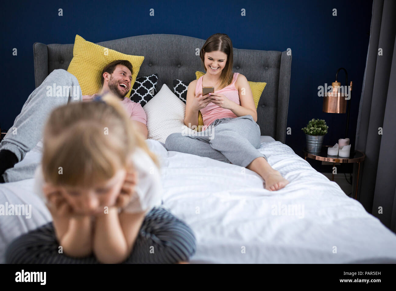 Négligé petite fille assise sur le lit avec ses parents, using smartphones Banque D'Images
