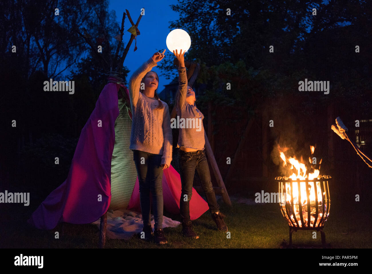 Deux filles debout en face de tipi, holding lampe comme lune Banque D'Images Deux filles debout en face de tipi, holding lampe comme lune Banque D'Images
