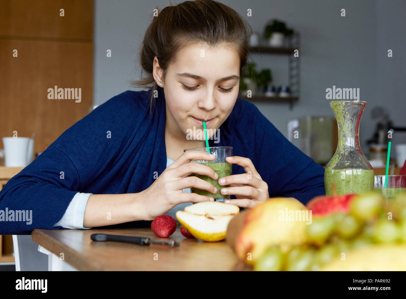 Fille assise dans la cuisine, boire smoothie aux fruits faits maison Banque D'Images