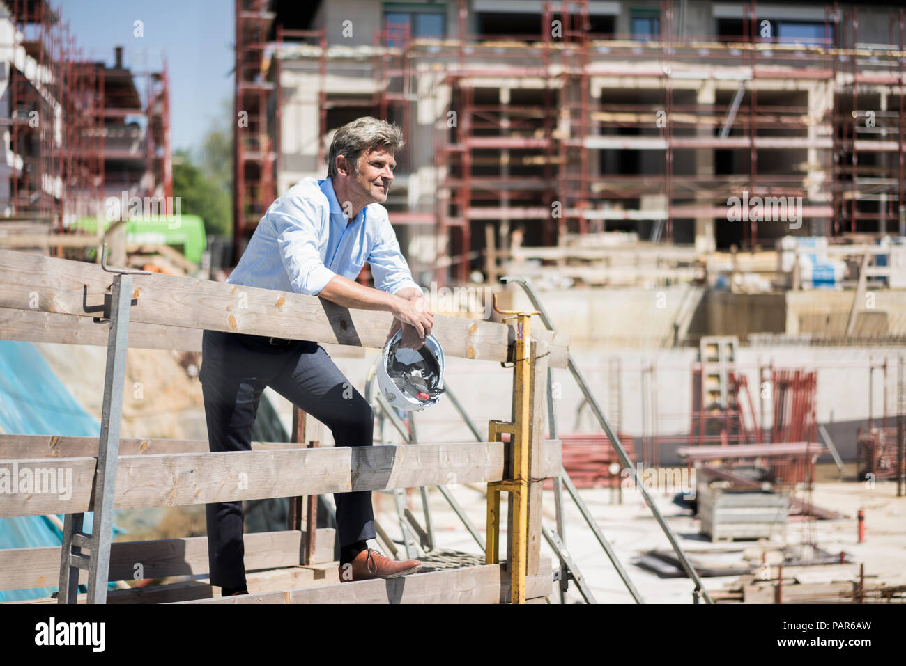 Smiling man holding hard hat le site de construction à la recherche autour de Banque D'Images