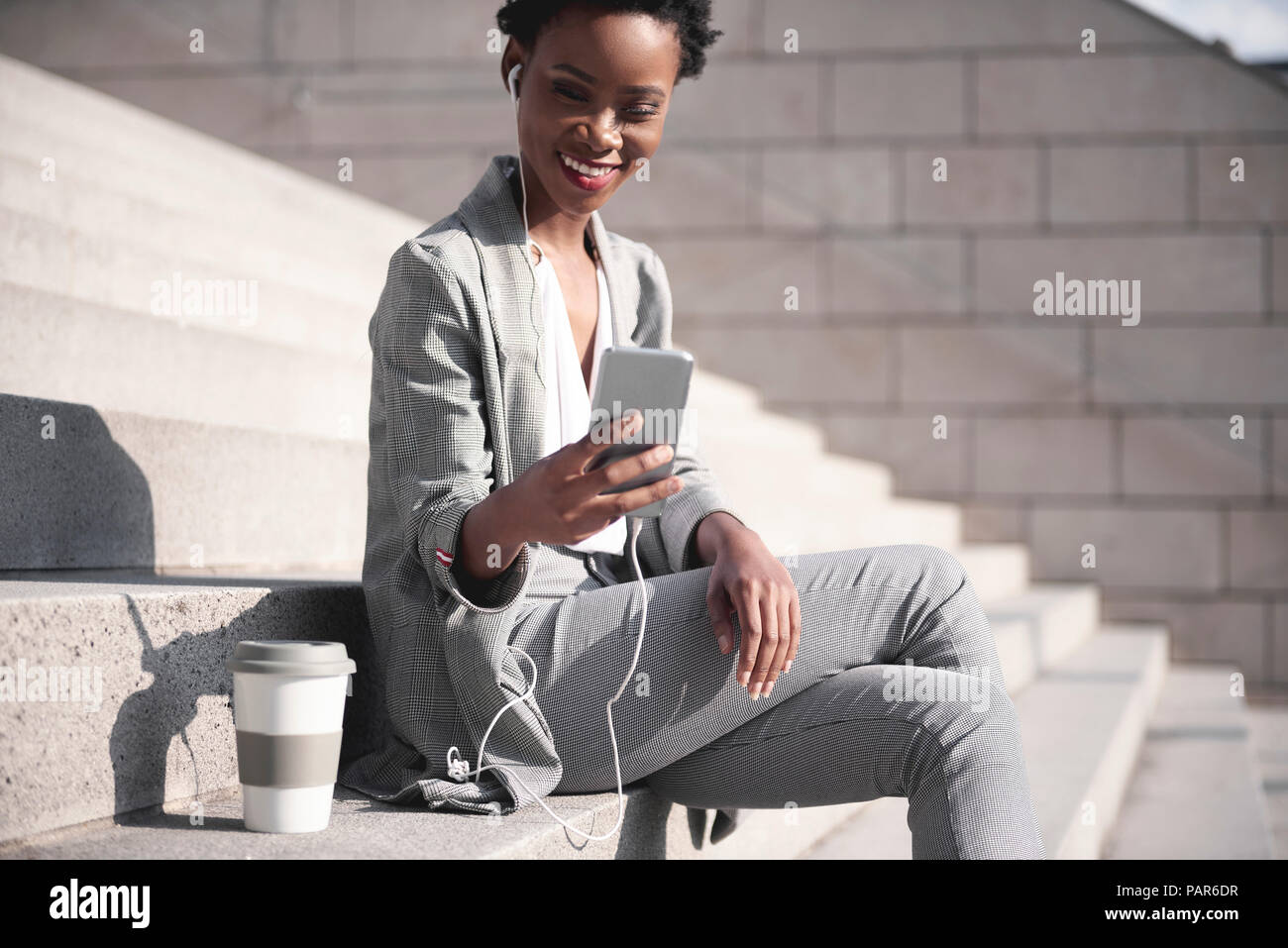 Portrait of smiling businesswoman sitting on stairs en utilisant des écouteurs et smartphone Banque D'Images