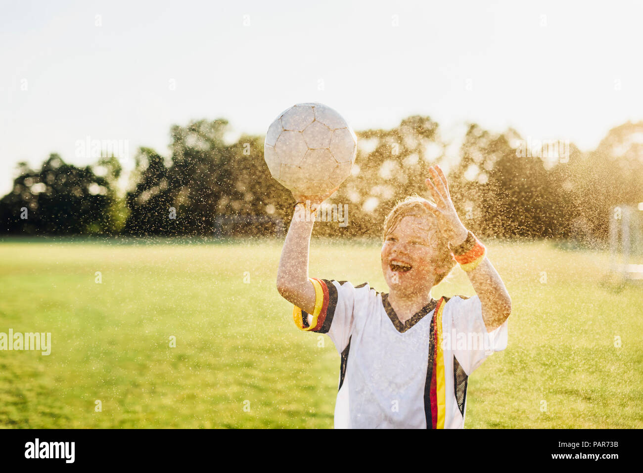 Boy wearing German soccer shirt crier de joie, debout dans les projections d'eau Banque D'Images