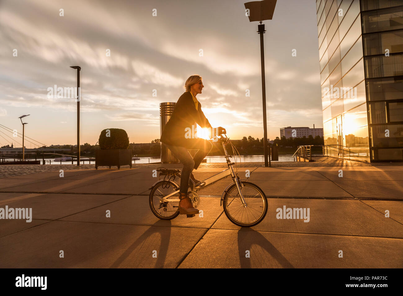 Senior woman riding vélo de ville au bord du fleuve au coucher du soleil Banque D'Images