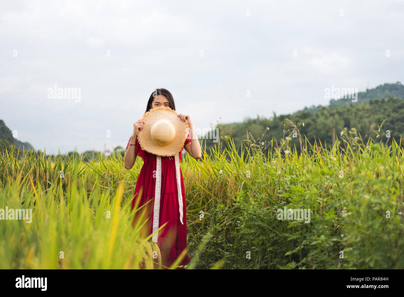 Jeune fille dans un champ de riz portant robe rouge et un chapeau Banque D'Images
