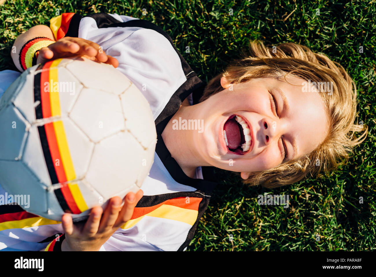 Garçon en allemand soccer shirt allongé sur l'herbe, riant joyeusement Banque D'Images
