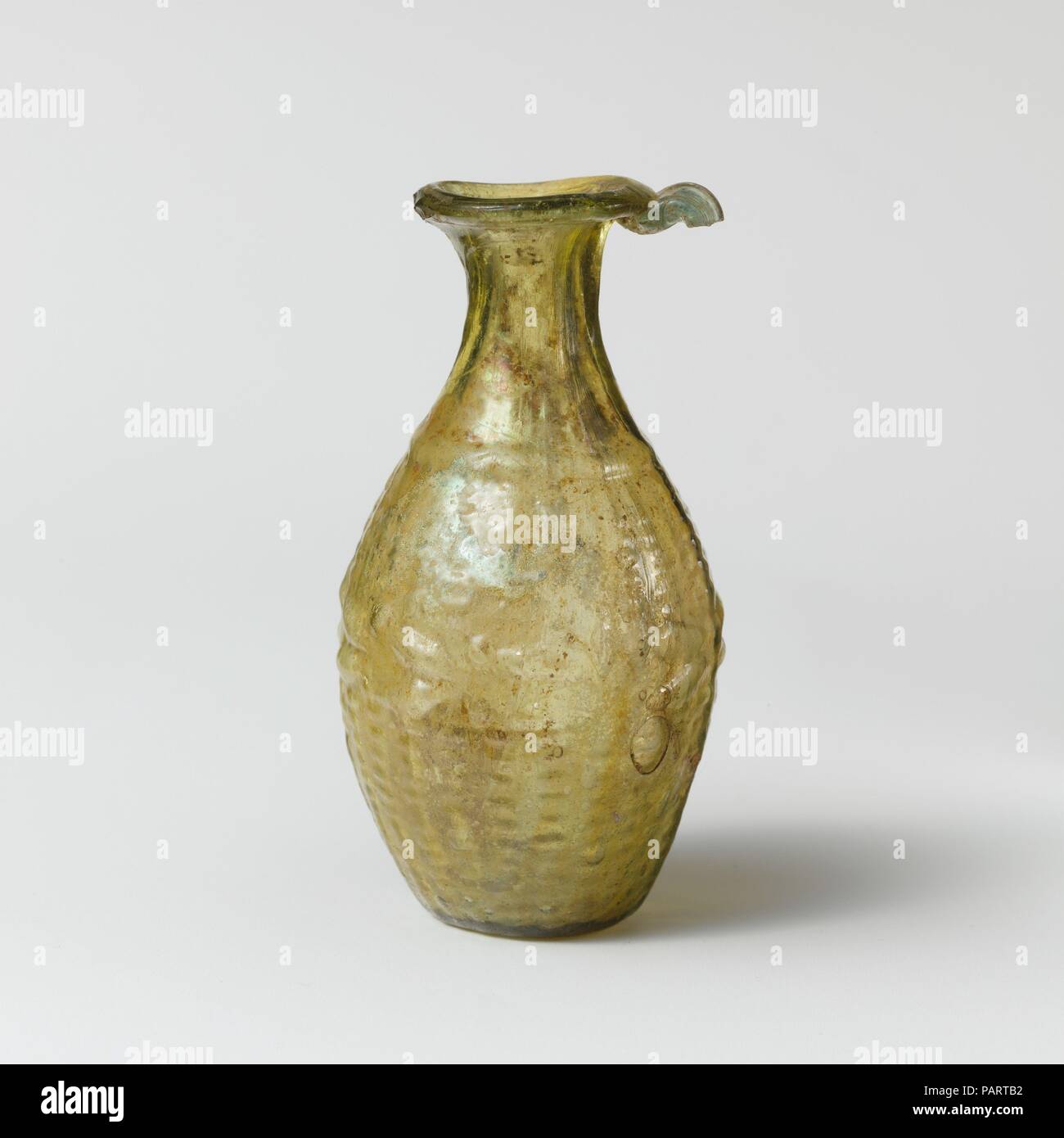 Amphoriskos en verre (flacon). Culture : Roman. Dimensions : H. : 3 7/16 in. (8,7 cm). Date : 1ère moitié du 1er siècle de notre ère. Jaune translucide vert, bleu pâle avec poignée verte. Inégale, épaisse, ovale, rim déployés, sur et dans, puis transformées en bouche du torchage côté concave ; cou l'expansion dans l'épaule ; corps ovoïde ; base circulaire à fond plat ; Poignée de tige appliqué sur le dessous de la jante et tiré vers le bas. Une seule couture moule autour de corps et l'ensemble bas, s'étendant jusqu'à la jante et formant des crêtes épaisses à côtés du cou et une ligne de fond soulevées dans l'ensemble. La forme d'une miniature stor Banque D'Images