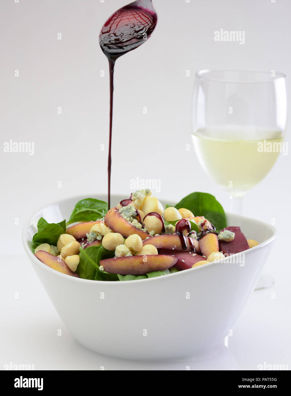 Noisettes et salade d'épinards avec vinaigrette rouge tomber sur elle et un verre de vin blanc Banque D'Images