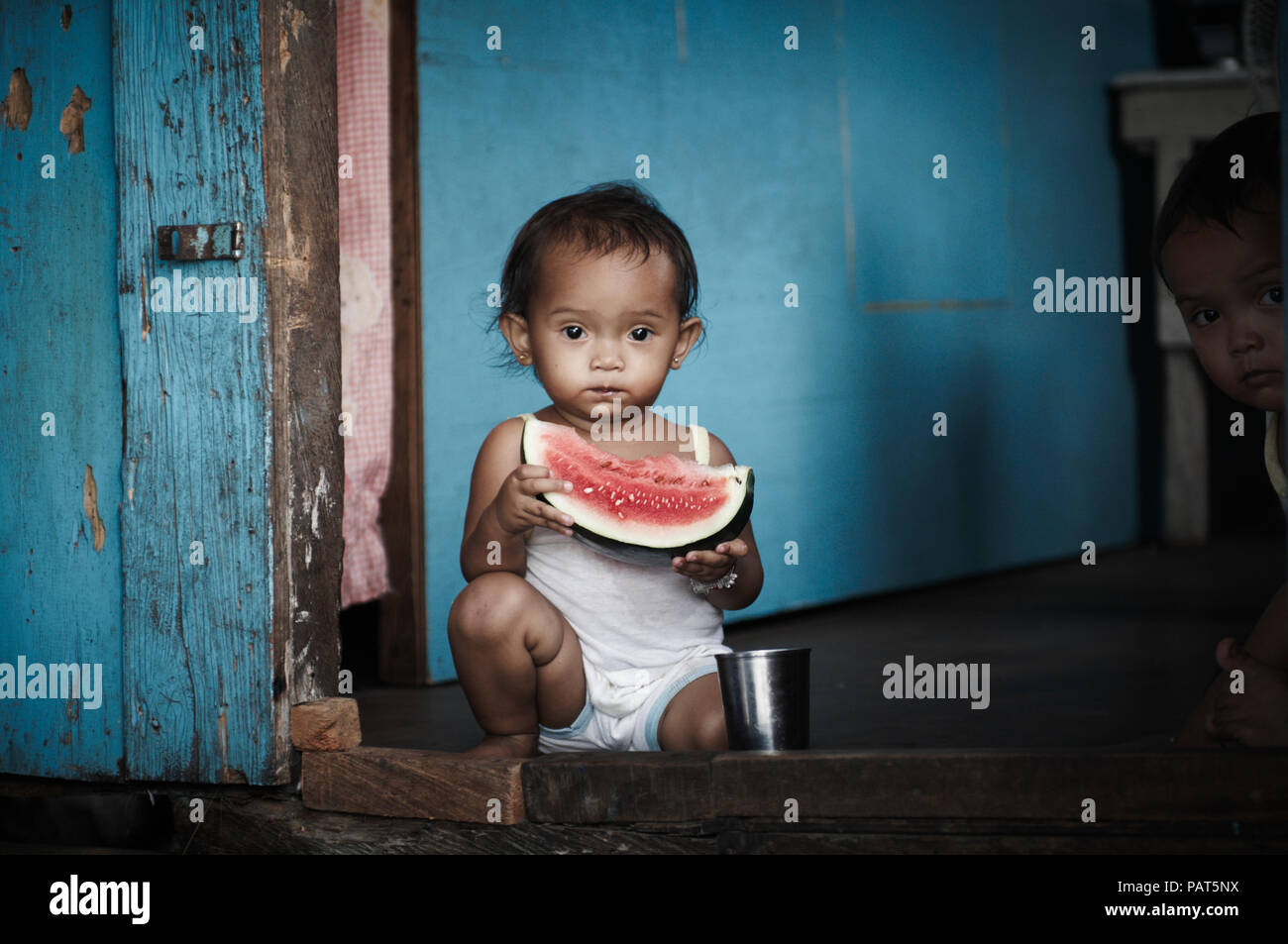 Une petite fille mange de la pastèque dans sa maison. Banque D'Images