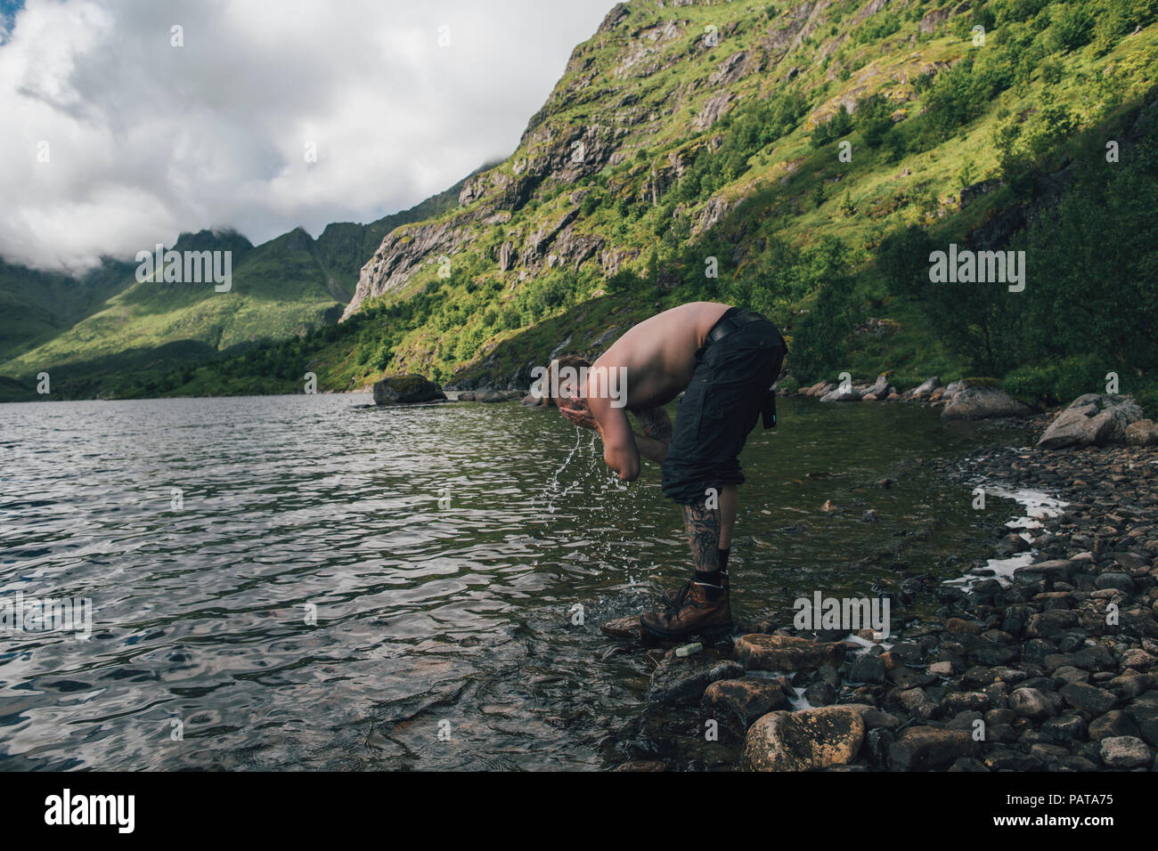 La Norvège, les îles Lofoten, Moskenesoy, jeune homme lave son visage dans Agvatnet lake Banque D'Images