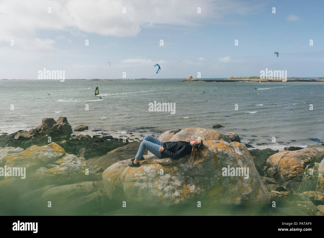 France, Bretagne, Landeda, young woman wearing headphones lying on rock at the coast Banque D'Images