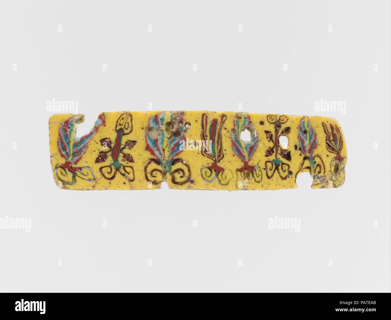 Incrustation en mosaïque de verre. Culture : l'Egyptien, Roman. Dimensions : d'autres : 1 3/4 in. (4,4 cm). Date : premier siècle avant J.-C. au 1er siècle de notre ère. Jaune opaque ; décoration en opaque, blanc, rouge et vert gris, translucide et deep purple apparaissant en noir. Bande horizontale étroite, légèrement obliques vers la droite et arrondie bord droit. Motif floral répétitif asymétrique avec boutons de lotus, de palmettes, flanqué de quatre tiges et feuilles de lierre. Cassé et réparé avec quelques fissures et des pertes ; face inférieure, supérieure, et les bords et polie ; piqûres profondes de quelques bulles en surface. Ce morceau est découpé dans le Banque D'Images