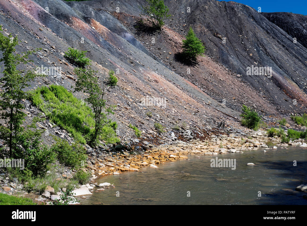 Déchets de résidus de mine de charbon le tas de déblais à côté d'un ruisseau à l'orange rochers montrant les dommages environnementaux de la pollution toxique et le drainage minier acide. Banque D'Images