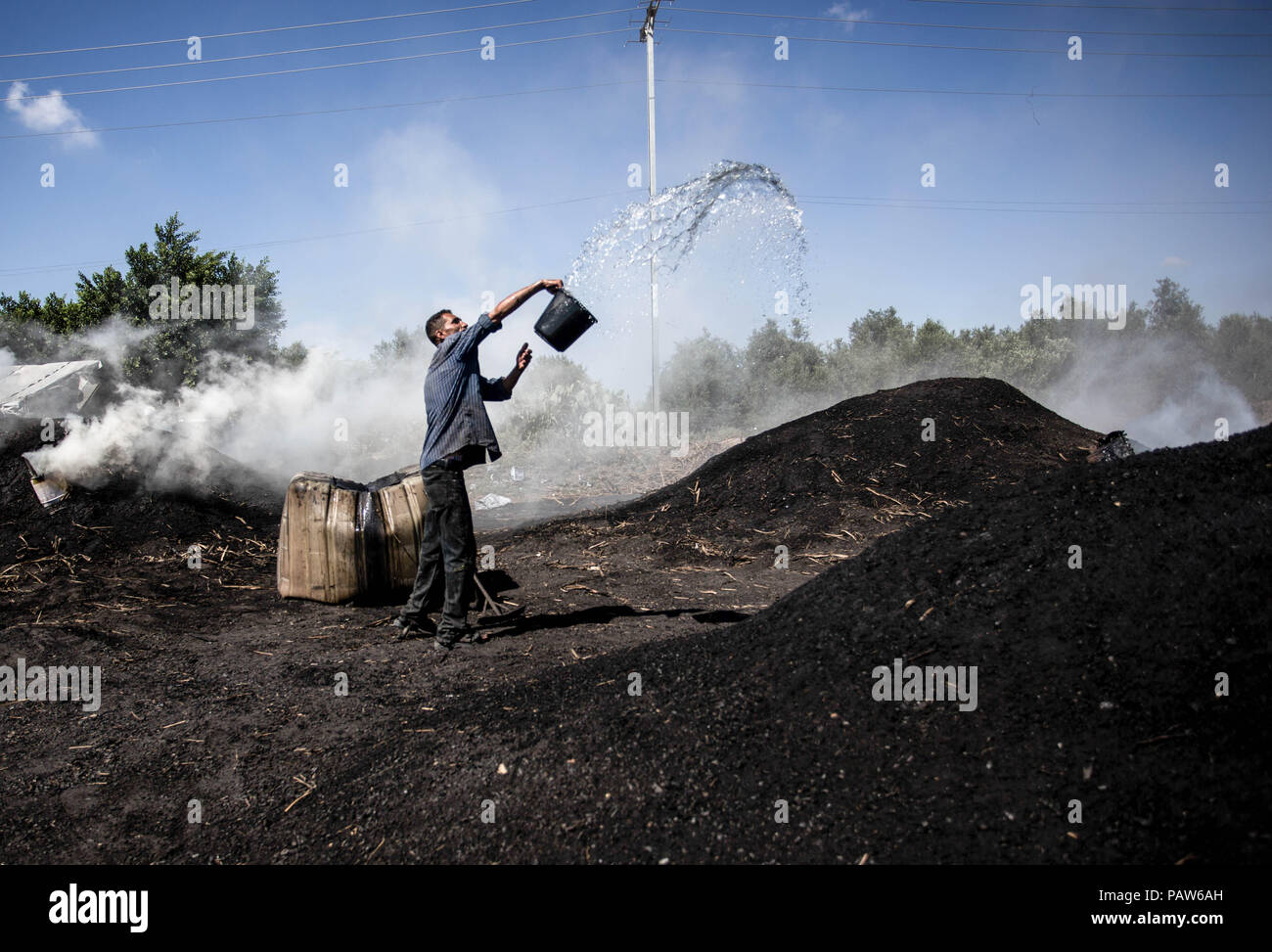 La ville de Gaza, en Palestine. 11 juillet, 2018. Travailleur palestinien vu verser de l'eau sur la combustion du charbon, l'extraction de charbon.le sable à l'Al Habbash usine de production, le plus grand producteur de charbon dans la bande de Gaza. Il est habituellement utilisé par les Palestiniens pour des raisons pratiques, telles que la cuisine et le chauffage. Un kilo est vendu pour $ 1,50 2,00 $ sur place et sur le marché. Credit : Mahmoud Issa/SOPA Images/ZUMA/Alamy Fil Live News Banque D'Images