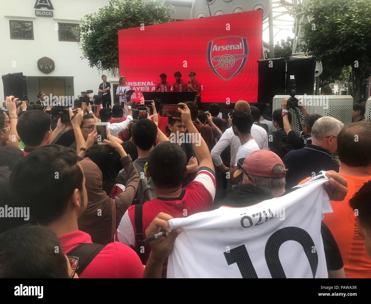 25 juillet 2018, à Singapour : football, Arsenal FC conférence de presse. Mesut Özil (arrière-R) est assis sur le podium avec l'équipe tandis que quelqu'un dans le public montre un jersey de la nationale de football allemand. Arsenal FC est actuellement sur un tour de la publicité en Asie. Le club de Londres se réunira l'Atlético Madrid et Paris Saint-Germain en leur présence dans la ville du sud-est asiatique à l'état de la Coupe des Champions internationaux. Photo : Christoph Sator/dpa Banque D'Images