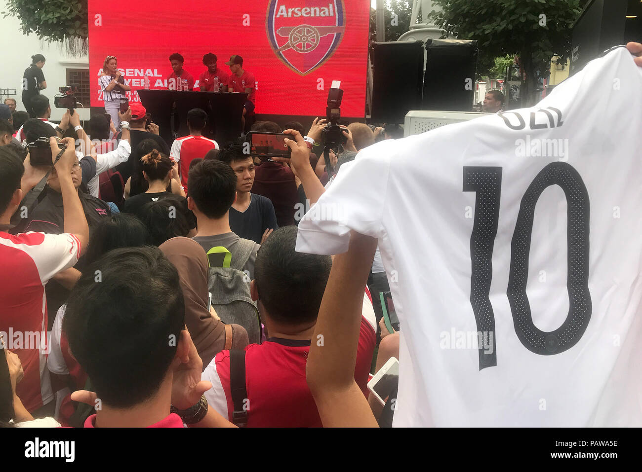25 juillet 2018, à Singapour : football, Arsenal FC conférence de presse. Mesut Özil (arrière-R) est assis sur le podium avec l'équipe tandis que quelqu'un dans le public montre un maillot national du footballeur allemand. Arsenal FC est actuellement sur un tour de la publicité en Asie. Le club de Londres se réunira l'Atlético Madrid et Paris Saint-Germain en leur présence dans la ville du sud-est asiatique à l'état de la Coupe des Champions internationaux. Photo : Christoph Sator/dpa Banque D'Images