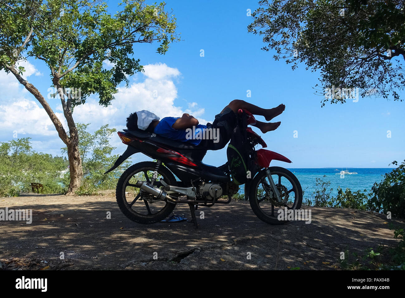 Alona Beach, Bohol - Philippines - local non identifié, l'homme dort sur le haut de sa moto près de la mer, protégeant le visage du soleil. Banque D'Images
