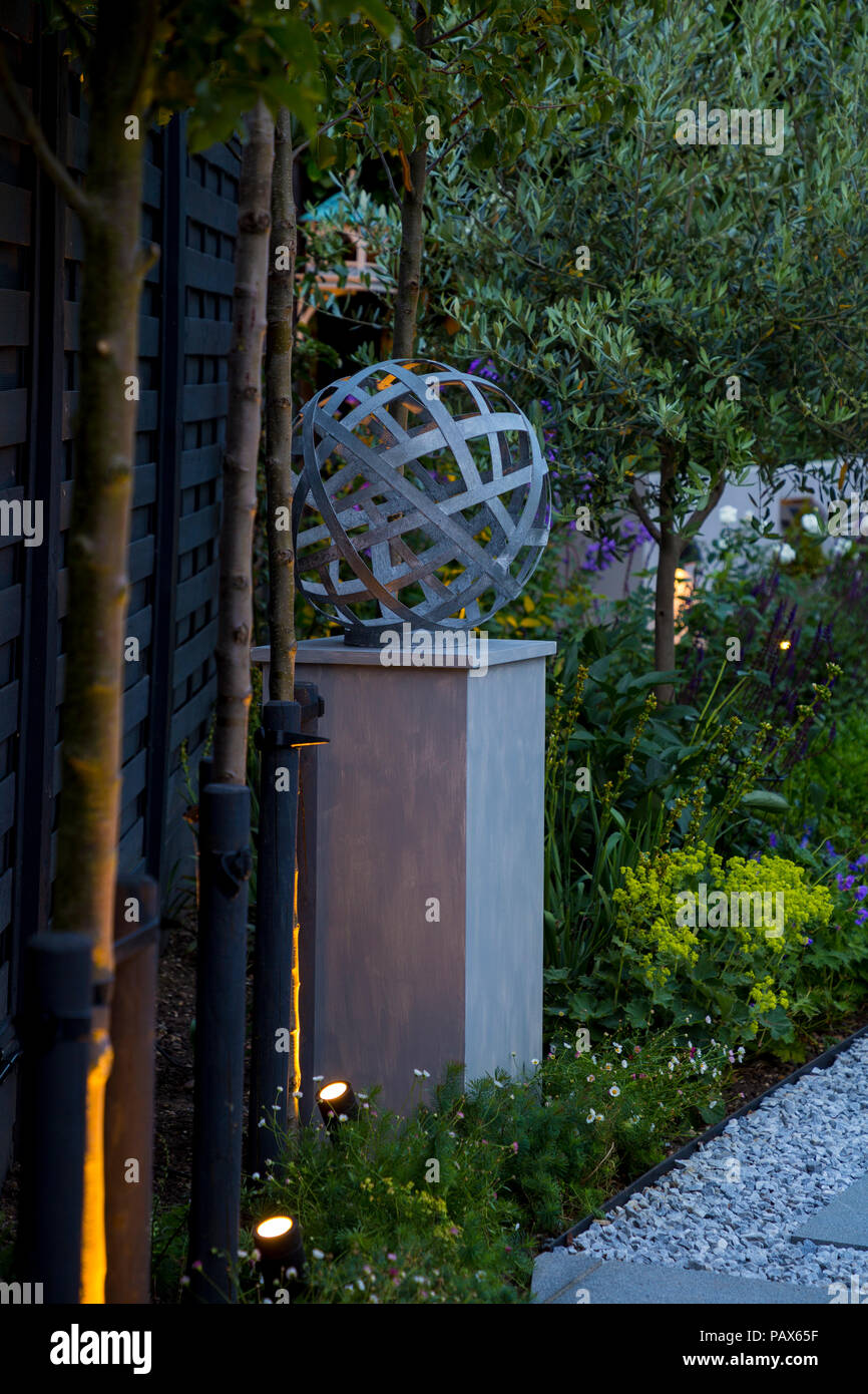 Une sculpture sphérique monté sur un socle en tant que point focal, avec uplighting Pyrus calleryana Chanticleer contre 'arbres' Banque D'Images