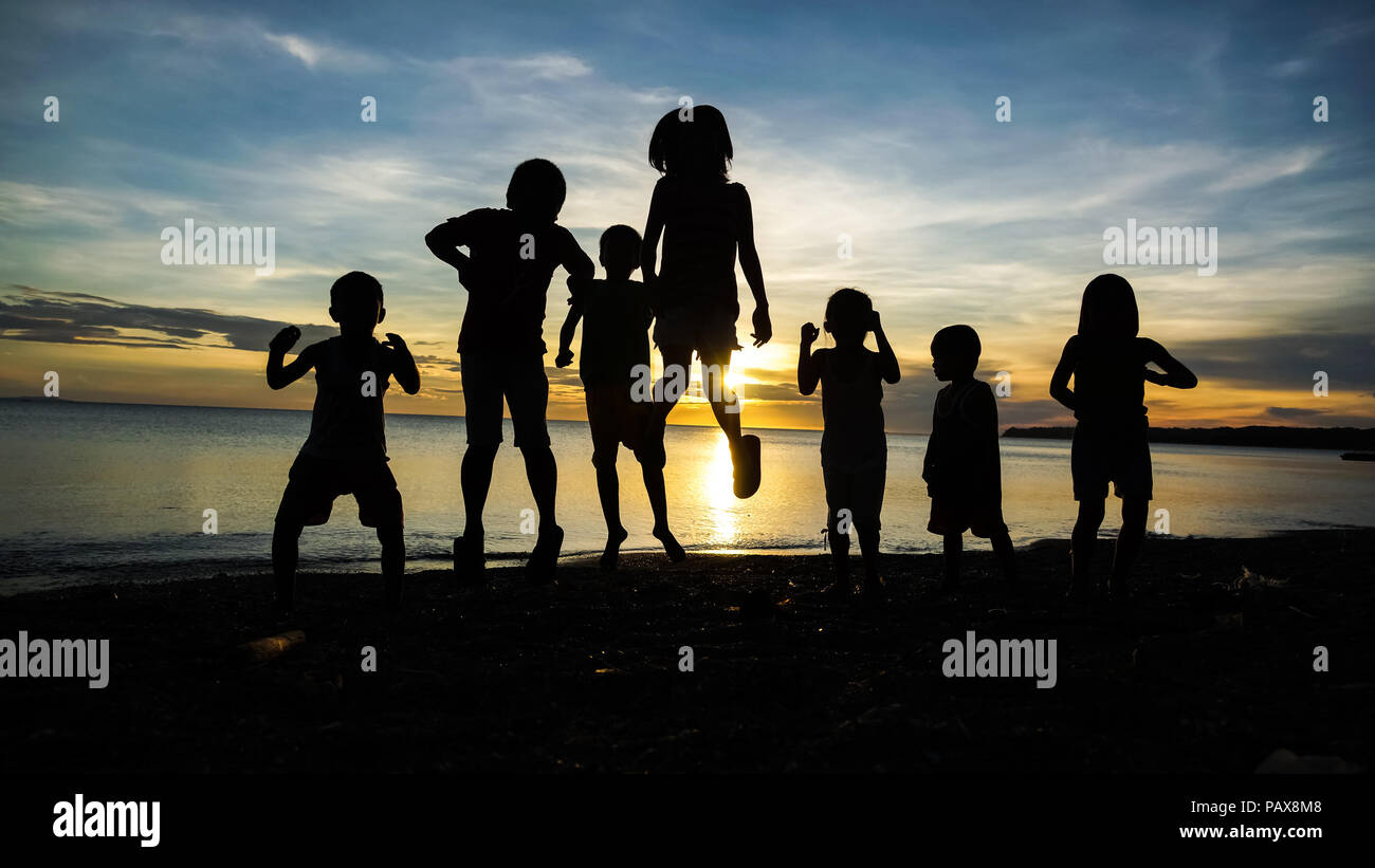 Les enfants du village de Silhouette groupe sautant et jouant sur un lever de Island Beach Banque D'Images