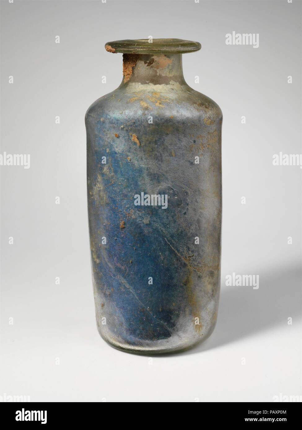 Bouteille cylindrique en verre. Culture : Roman. Dimensions : H. : 5 1/2 in. (14 cm). Date : fin 1re et 2e siècle de notre ère. Teinte de vert incolore. Jante tubulaire, dépliées, légèrement vers le bas, rond, et en formant, bouche ovale inégale ; cou cylindrique court, oblique ; corps cylindrique avec côtés verticaux ; fond concave. Piqûre intact ; et quelques bulles plus tard ; parcelle de sol rougeâtre l'incrustation sur le cou et le dessous de la jante sur l'extérieur, la plupart de l'intérieur recouvert d'incrustations du sol, les intempéries, et iridescence brillant. Musée : Metropolitan Museum of Art, New York, USA. Banque D'Images