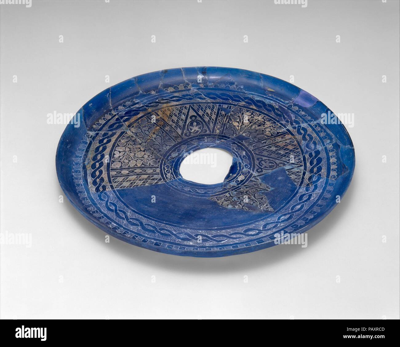 Plaque fragmentaire avec dessins gravés. Dimensions : H. ca. 9/16 in. (Ca. 1,5 cm) Diam. En 11. (28 cm). Date : 9ème siècle. La couleur bleu de cette plaque a été obtenu par l'ajout de cobalt au tissu de verre, et sa surface a été gravé de différents motifs disposés en registres concentriques autour d'une cocarde. L'orifice circulaire au centre indique le lieu où un pied était une fois attaché. Cette plaque est une preuve importante du commerce verre actif d'ouest en est au cours de la neuvième et dixième siècles. Probablement fabriqué en Syrie, il a été importé à Nishapur où il a été trouvé que je Banque D'Images