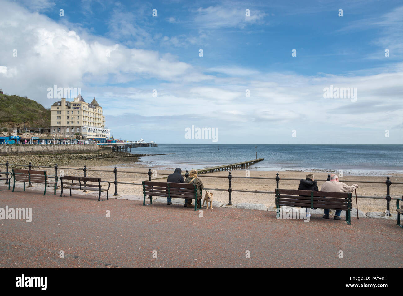 Les touristes assis sur des bancs face à la mer à Llandudno sur la côte du nord du Pays de Galles, Royaume-Uni. Banque D'Images